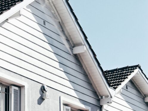 White house exterior with a sharply angled roof and black shingles under a clear blue sky