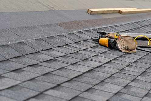 A close-up of newly installed asphalt shingles and roofing tools, including a nail gun