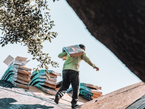 Roofer carrying a bundle of shingles up a roof during construction