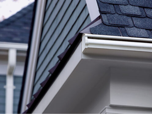 A dark gray shingle roof with a white seamless gutter system and crisp siding