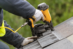 roofer using a nail gun to nail down asphalt shingles