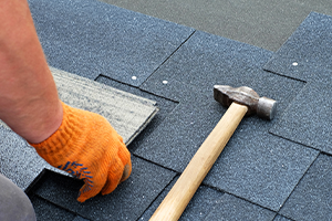 roofer laying asphalt shingles with a hammer laying next to his work