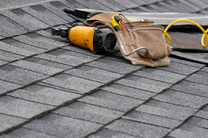nail gun and tool belt laying on an asphalt roof