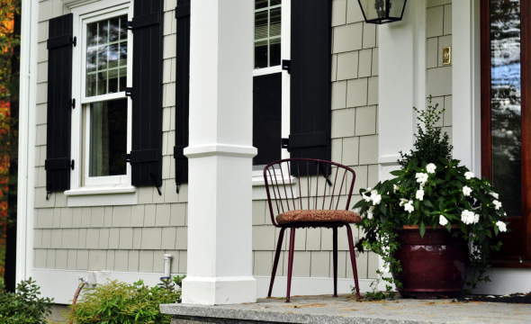 A welcoming porch with black window shutters, a small chair, and potted plants